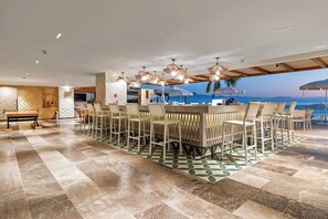 Uma ampla área de refeições interna com uma mesa comprida e cadeiras, um balcão de bar e vista para o oceano.