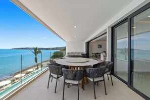 Un espace repas extérieur moderne, doté d’une table ronde et de chaises, offrant une vue sur la côte et un ciel dégagé.
