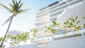 A modern hotel with multiple floors, outdoor seating areas, and a palm tree. - Panarea 2C: Lux Beachfront 3BR, Oceanviews + Pools (Bucerías)