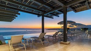 An infinity pool with lounge chairs and umbrellas, overlooking a sunset over the ocean. - Panarea 2C: Lux Beachfront 3BR, Oceanviews + Pools (Bucerías)