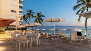 A beachfront patio with tables and chairs, umbrellas, and a pool. - Panarea 2C: Lux Beachfront 3BR, Oceanviews + Pools (Bucerías)