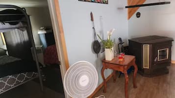 A room with a bunk bed, a fan, a small table with a plant, and a wood-burning stove.