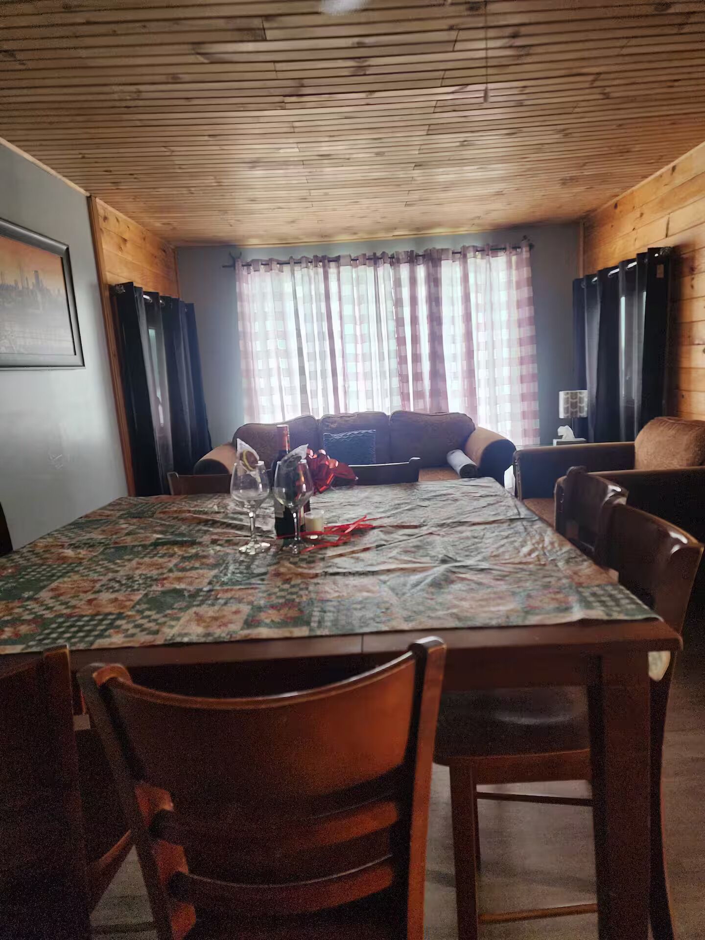 A dining area with a table set for two, a sofa, and a window with curtains.