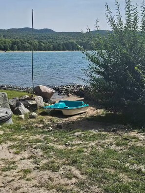 A boat on a sandy shore with a body of water and hills in the background.