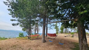 A hammock swing set with a red hammock and two blue swings, set against a backdrop of trees and a view of the water.