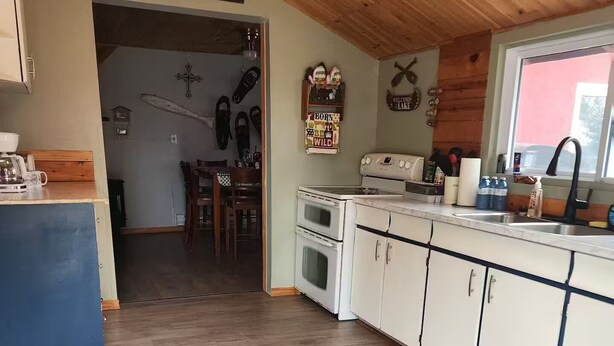 A kitchen with wooden cabinets, a stove, and a window. There is a rug on the floor and a ceiling fan.