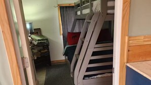 A bunk bed with a wooden ladder, a small desk with a lamp, and a curtain.