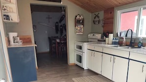 A kitchen with wooden cabinets, a ceiling fan, and a view of a dining area.