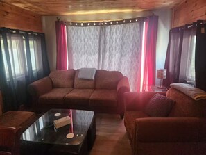 Ein gemütliches Wohnzimmer mit einer Couch, Sesseln, einem Couchtisch und Vorhängen.