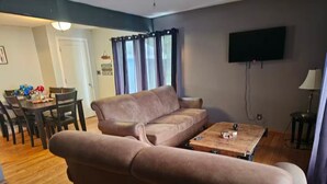 A living room with a sofa, a coffee table, a TV, and a dining area with chairs and a table.