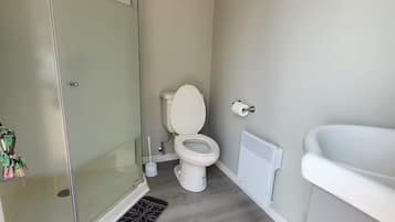 Een badkamer met een douchecabine van glas, een toilet, een radiator en een wastafel.