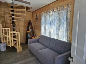Una habitación con una escalera de madera, un sofá gris y un ventanal con cortinas estampadas.