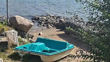 Een boot aan een zandstrand met een waterlichaam en heuvels op de achtergrond.