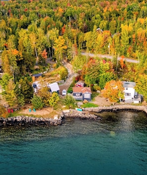 A residential area with houses surrounded by dense forest and a body of water.