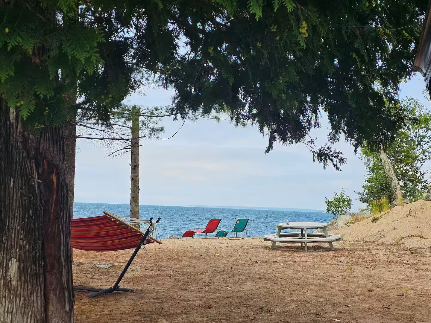 A beach with a hammock, picnic table, and chairs.