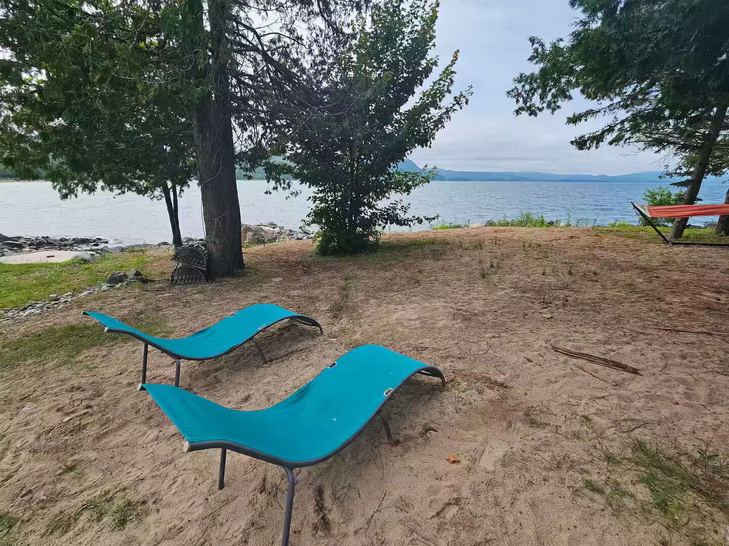 Une zone de plage avec deux chaises longues bleues, un banc rouge et une vue sur l’eau.