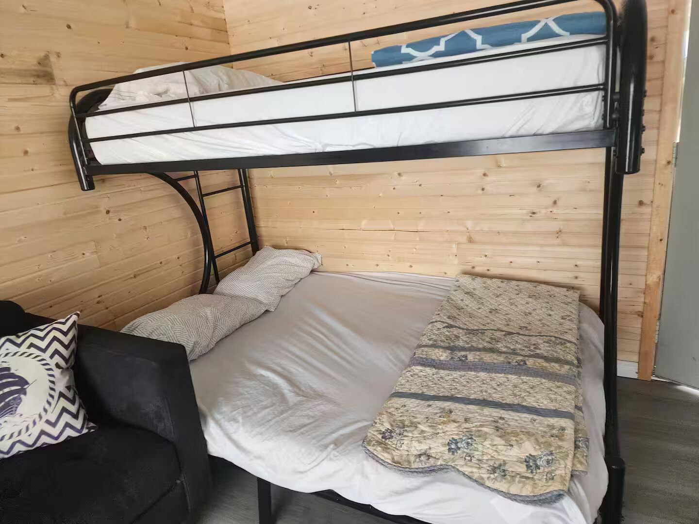 Un letto a castello con un giroletto inferiore e una testiera, adiacente a una parete di legno.