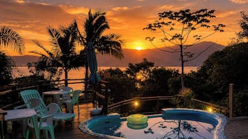 Vista do pôr do sol com piscina, cadeiras e mesa em um deck de madeira.