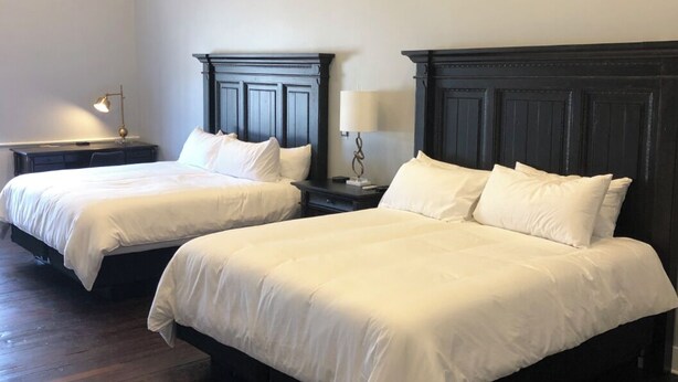 A hotel room with two beds, wooden flooring, and dark headboards. - The Royal on Main  (Batesville)