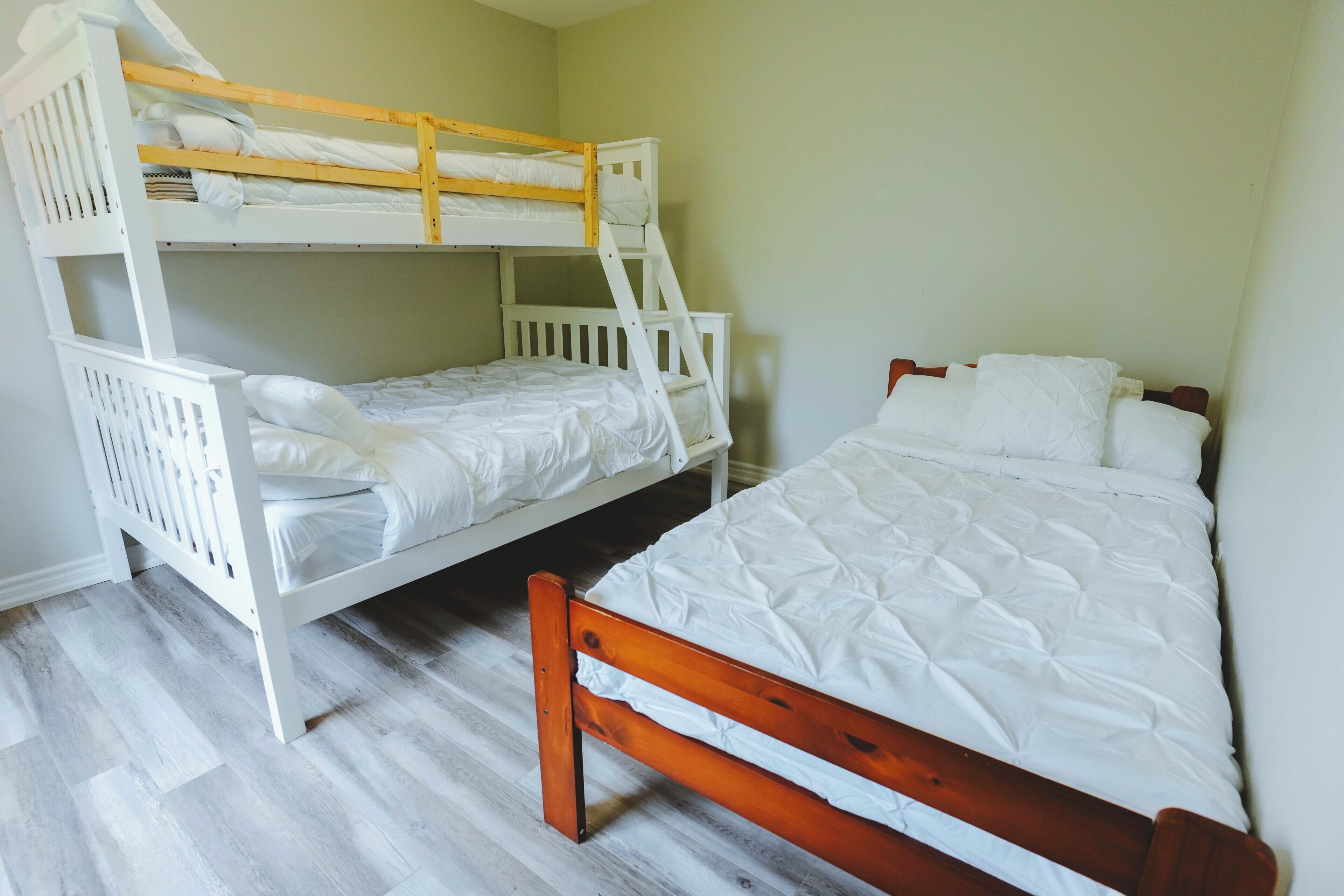 Une chambre avec deux lits superposés, l’un avec une structure en bois et l’autre avec une structure blanche, et les deux sont équipés de draps blancs.