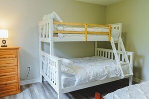 Ein Etagenbett mit weißer Bettwäsche, eine Holzkommode und eine Lampe.