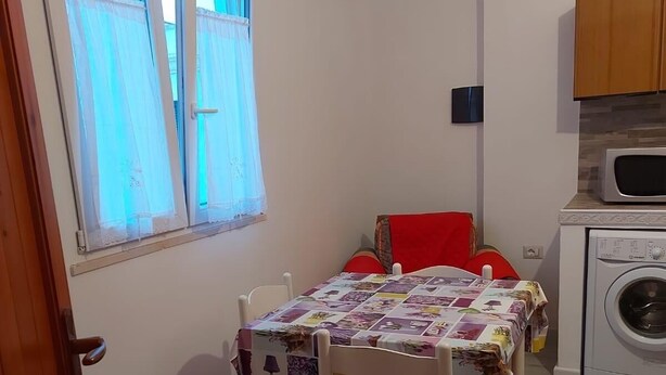 Une petite pièce avec une table et des chaises, une fenêtre avec des rideaux et un lave-linge.
