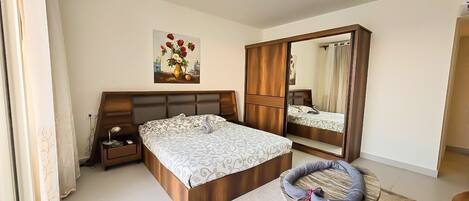 Une chambre à coucher avec un grand lit, une armoire, un miroir, une table de chevet et un fauteuil décoratif.