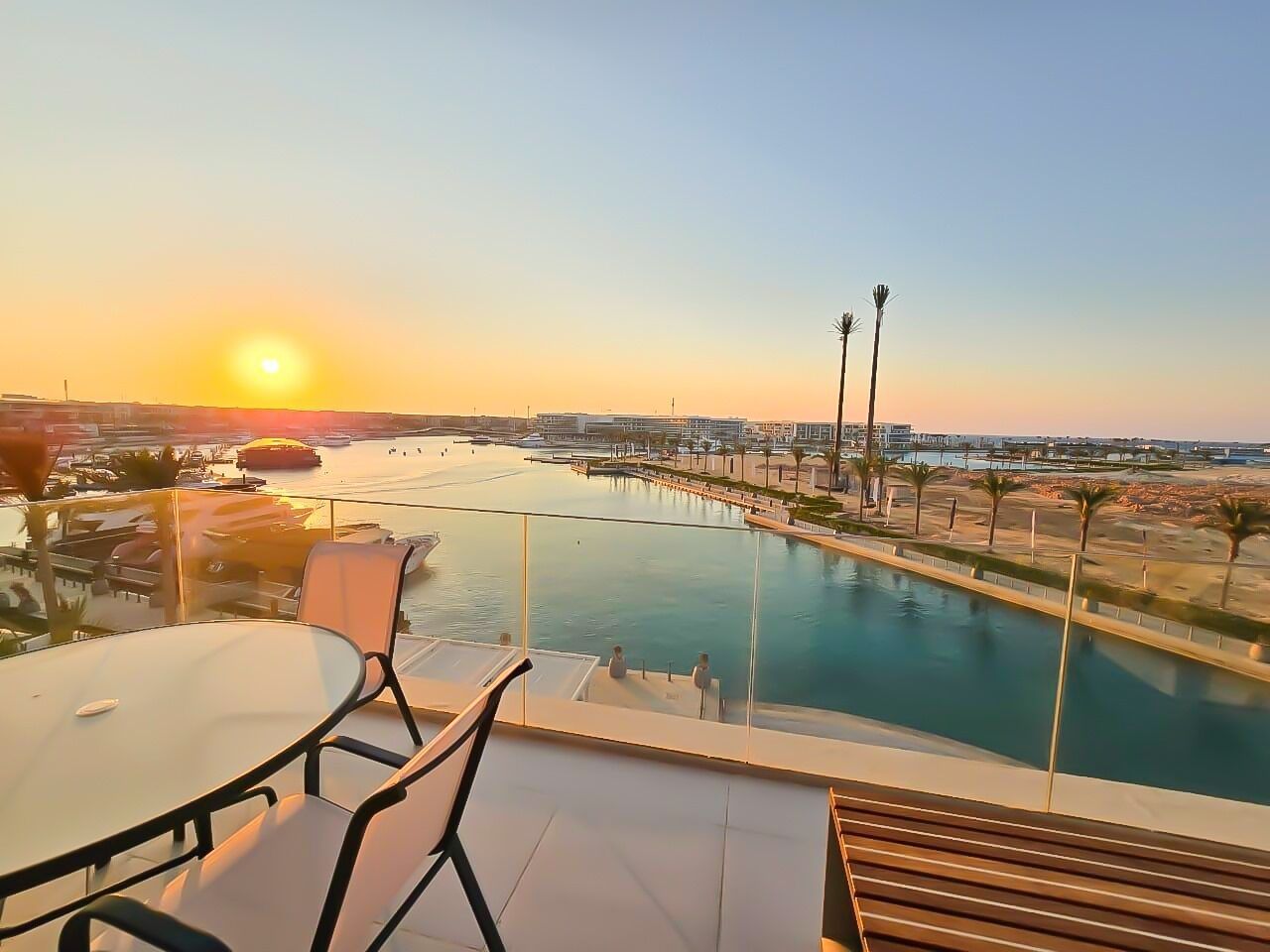 Terraza en la azotea con piscina, vista a un puerto deportivo y al paisaje urbano al atardecer.