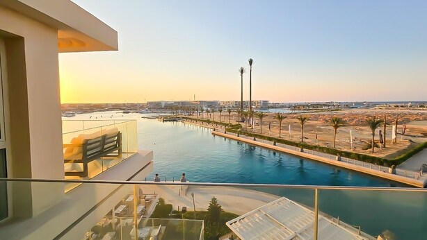 A balcony with a view of a marina, a pool, and a beach area.