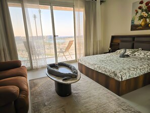 Ein Schlafzimmer mit einem Bett, einer Couch, einem kleinen Tisch und Blick ins Freie.