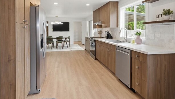 A modern kitchen with wooden cabinets, a stainless steel refrigerator, and a window providing natural light.