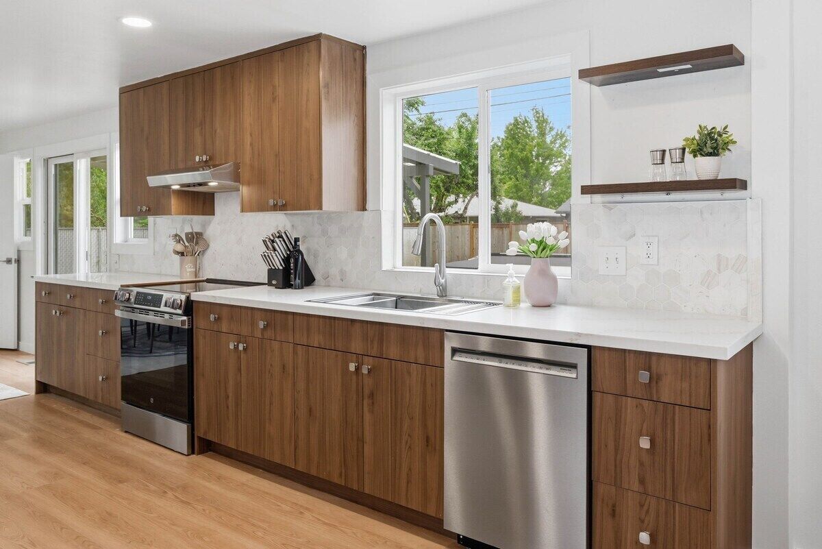 A modern kitchen with wooden cabinets, stainless steel appliances, a large window, and a countertop with a sink.