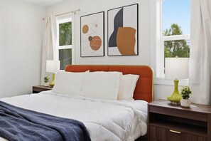 Ein Schlafzimmer mit einem Bett, einem Nachttisch, einer Lampe und einem Fenster.