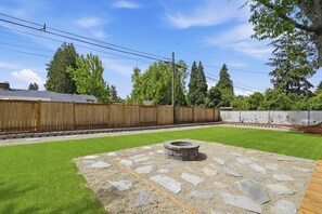 A backyard with a stone fire pit, a wooden fence, and a grassy lawn. - Private Hot Tub, Game Room, Near UO & Autzen (Eugene)