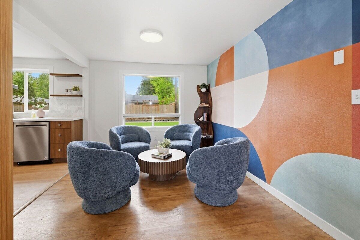 A modern living room with a round coffee table, four blue armchairs, and a large abstract mural on the wall.