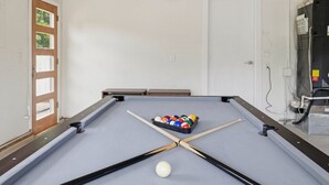 A pool table with a cue ball and a set of billiard balls, a door, and a wall-mounted air conditioning unit.