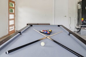 Ein Billardtisch mit einer weißen Billardkugel und einem Satz Billardkugeln, eine Tür und ein wandmontiertes Klimagerät.