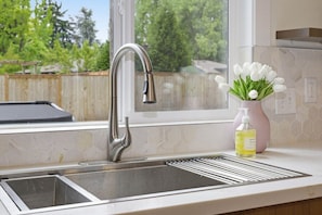 A kitchen sink with a modern faucet, a window with a view of trees, and a vase with white flowers on the counter. - Private Hot Tub, Game Room, Near UO & Autzen (Eugene)