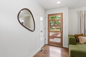 A hallway with a wooden door, a round mirror, and a green sofa with cushions. - Private Hot Tub, Game Room, Near UO & Autzen (Eugene)