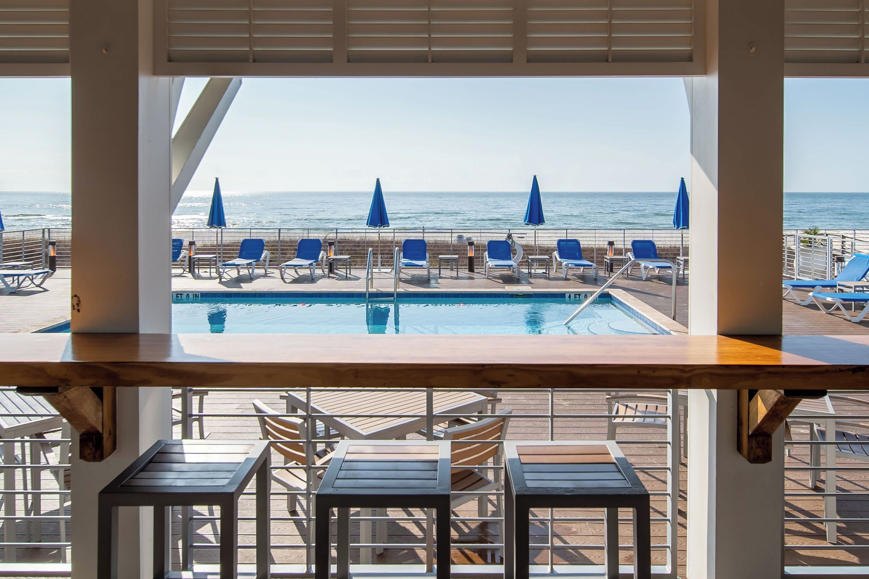 A poolside area with lounge chairs and umbrellas, overlooking a beach and ocean.