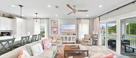A spacious living area with a sofa, coffee table, and a television. There is a balcony with outdoor seating.