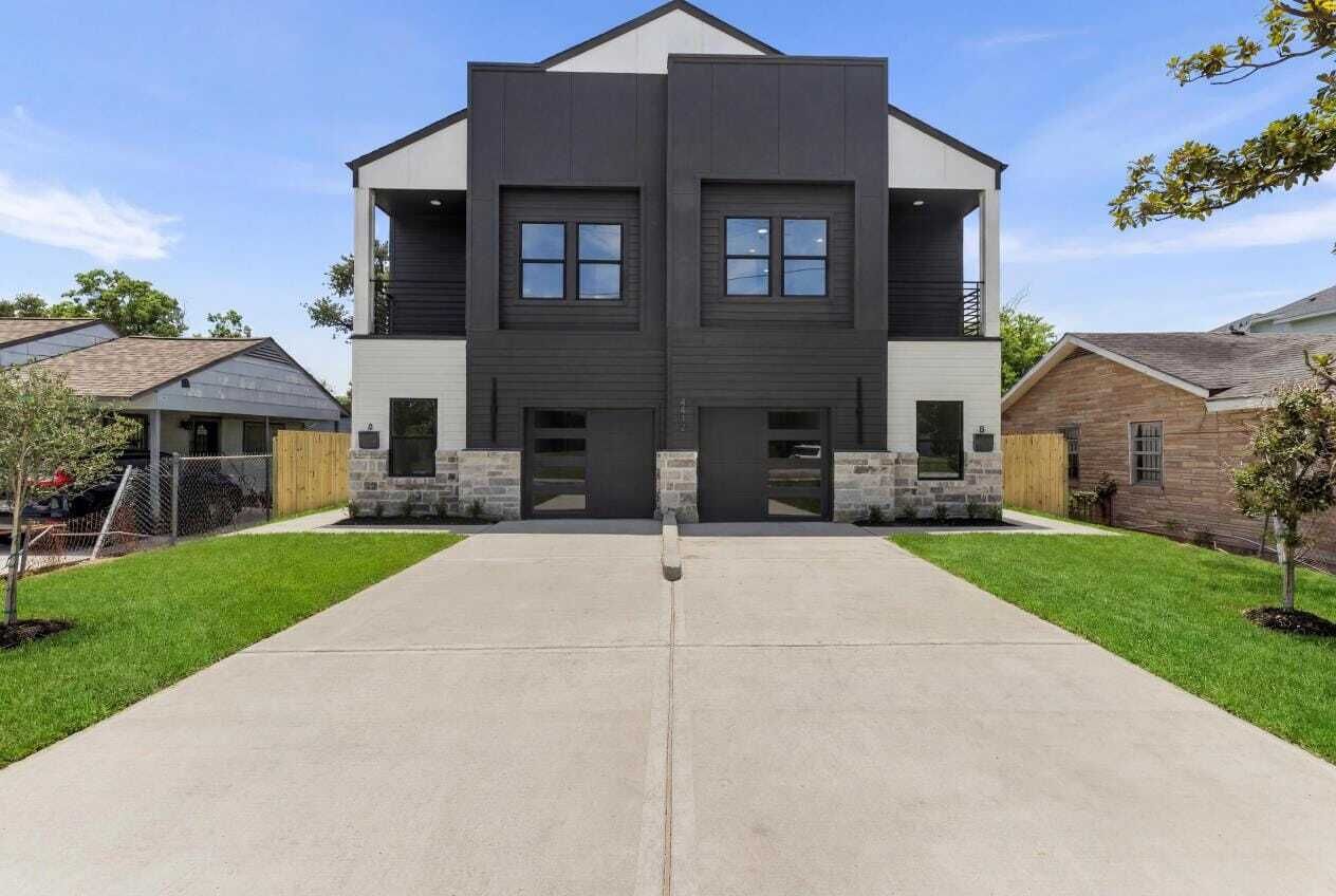 A modern two-story house with a concrete driveway, stone accents, and a symmetrical facade.