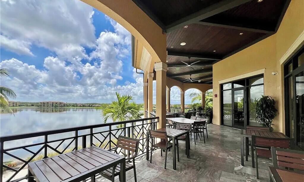 An outdoor patio with tables and chairs, overlooking a body of water and a clear sky.