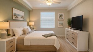 Quarto com cama, mesas de cabeceira, televisão e ventoinha no teto.