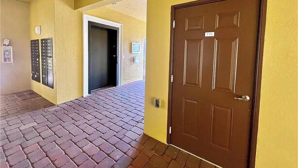 Um corredor com uma porta marrom, sistema de entrada por teclado e piso de tijolos.
