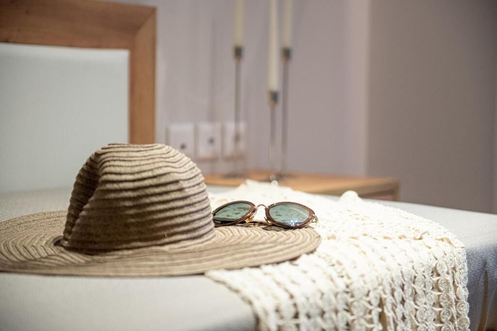 A bed with a striped hat and glasses on a white blanket.