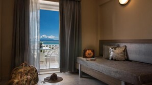 Habitación de hotel con una cama, una maleta, un sombrero y vista a la playa por la ventana.