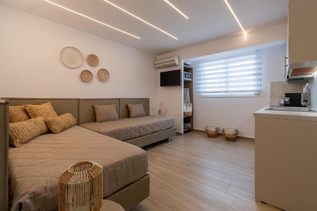 A modern room with a bed, a sofa, a small kitchen area, and a window with blinds.