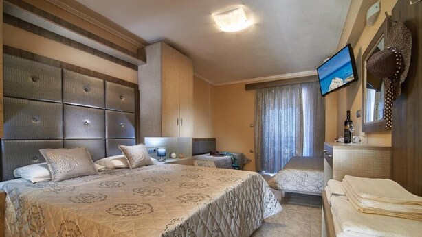 Habitación de hotel con una cama grande, un televisor montado en la pared, un escritorio con una silla y una ventana con cortinas.