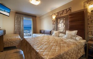 Una habitació d'hotel amb un llit gran, un altre més petit, una taula de treball i vista al mar.